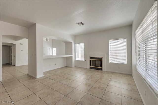 7977 Blue Brook Dr, Las Vegas, NV 89147 - unfurnished living room featuring a textured ceiling, light tile patterned floors, a glass covered fireplace, and arched walkways