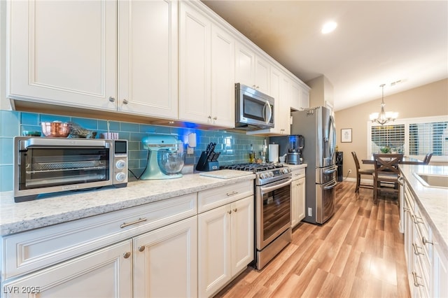 5733 Dazzling Sparks St, North Las Vegas, NV 89031 - kitchen with stainless steel appliances, backsplash, a chandelier, white cabinetry, and light wood-style flooring
