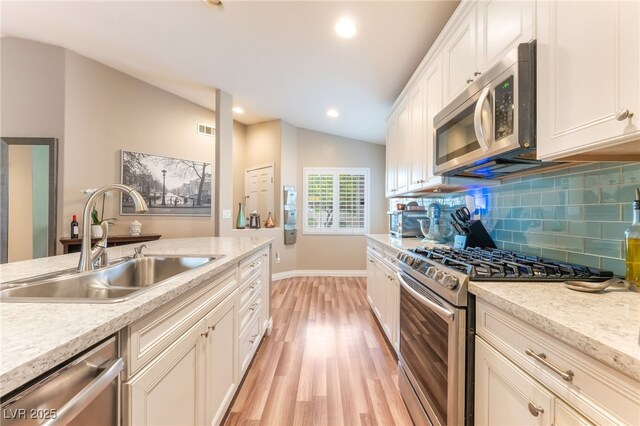5733 Dazzling Sparks St, North Las Vegas, NV 89031 - kitchen with stainless steel appliances, light wood-style floors, decorative backsplash, lofted ceiling, and white cabinets