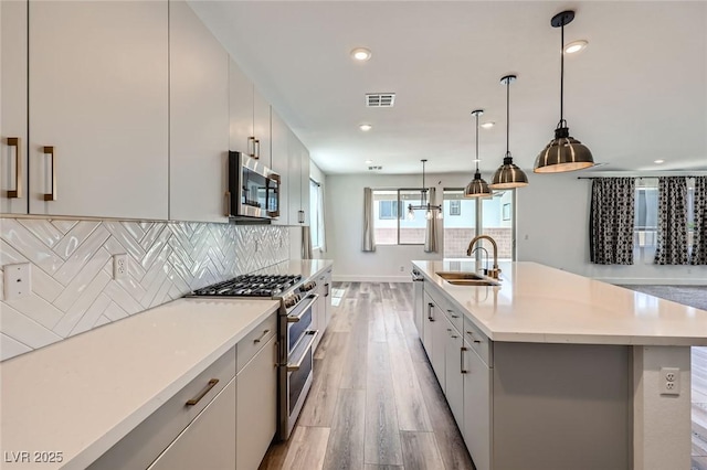 1213 Granite Falls Pl, North Las Vegas, NV 89084 - kitchen with stainless steel appliances, light wood-style floors, decorative backsplash, a center island with sink, and light countertops
