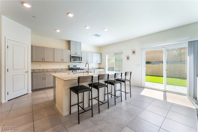 7211 Alabaster Peak St, Las Vegas, NV 89166 - kitchen featuring appliances with stainless steel finishes, gray cabinets, a breakfast bar, an island with sink, and light tile patterned floors