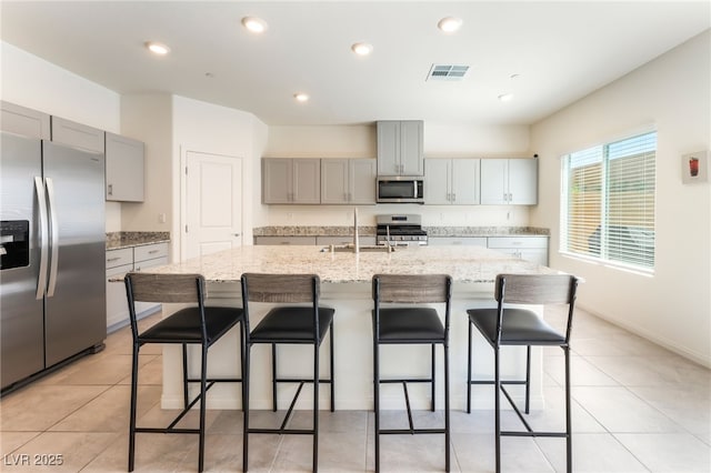 7211 Alabaster Peak St, Las Vegas, NV 89166 - kitchen featuring stainless steel appliances, gray cabinetry, a kitchen island with sink, light stone counters, and a breakfast bar area