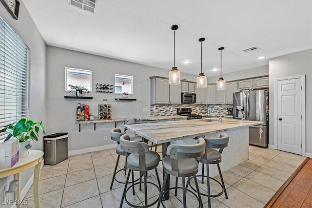 3591 Gloucester Gate St, Las Vegas, NV 89122 - kitchen with stainless steel appliances, gray cabinetry, tasteful backsplash, a kitchen breakfast bar, and a center island with sink