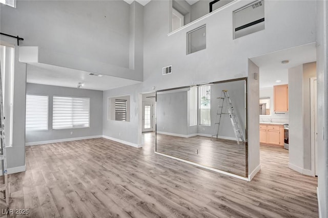 5823 Rose Sage St, North Las Vegas, NV 89031 - unfurnished living room featuring light wood-style flooring, a barn door, and a towering ceiling