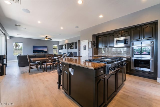 352 Angels Trace Ct, Las Vegas, NV 89148 - kitchen with appliances with stainless steel finishes, dark stone countertops, decorative backsplash, light wood-style floors, and a kitchen island