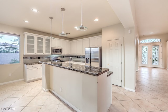 10300 Wellside Hill Ave, Las Vegas, NV 89145 - kitchen featuring appliances with stainless steel finishes, white cabinetry, light tile patterned floors, a kitchen island with sink, and dark stone countertops