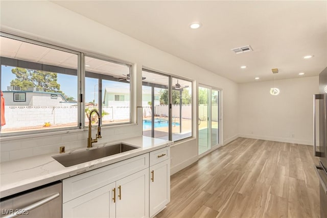 3748 Silent Hill Dr, Las Vegas, NV 89147 - kitchen with stainless steel dishwasher, white cabinets, light wood-style floors, light stone counters, and recessed lighting