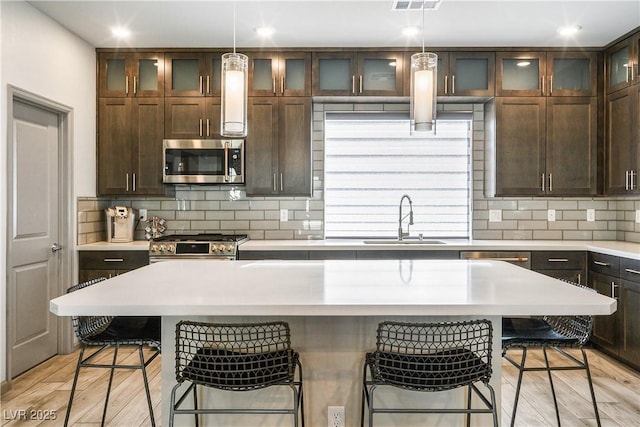 8175 Caldera Creek St, Las Vegas, NV 89113 - kitchen with stainless steel appliances, a kitchen bar, tasteful backsplash, dark brown cabinetry, and light countertops