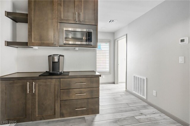 8175 Caldera Creek St, Las Vegas, NV 89113 - kitchen with stainless steel microwave, dark countertops, light wood-type flooring, dark brown cabinetry, and open shelves