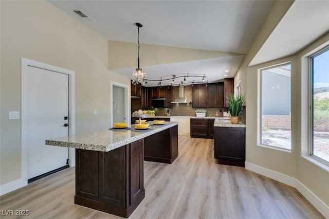 9800 Rosamond Dr, Las Vegas, NV 89134 - kitchen with stainless steel microwave, wall chimney exhaust hood, dark brown cabinetry, light wood finished floors, and a chandelier