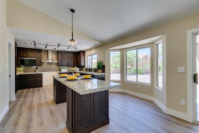 9800 Rosamond Dr, Las Vegas, NV 89134 - kitchen with stainless steel microwave, wall chimney range hood, dark brown cabinets, tasteful backsplash, and a center island