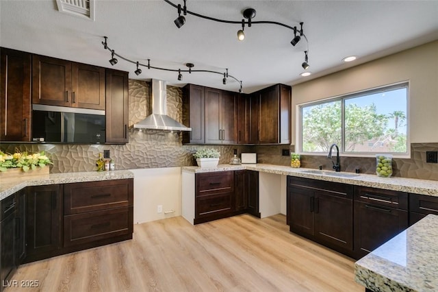 9800 Rosamond Dr, Las Vegas, NV 89134 - kitchen with wall chimney range hood, dark brown cabinets, light wood-type flooring, decorative backsplash, and light stone counters