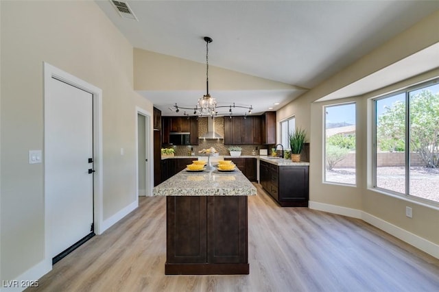 9800 Rosamond Dr, Las Vegas, NV 89134 - kitchen with wall chimney range hood, vaulted ceiling, a chandelier, decorative backsplash, and dark brown cabinetry