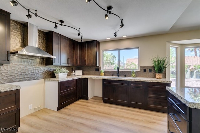 9800 Rosamond Dr, Las Vegas, NV 89134 - kitchen with wall chimney exhaust hood, dark brown cabinetry, backsplash, light wood finished floors, and recessed lighting