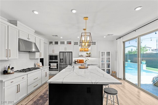 3369 Ponicelli Ln, Henderson, NV 89044 - kitchen with under cabinet range hood, stainless steel appliances, tasteful backsplash, light wood-type flooring, and recessed lighting