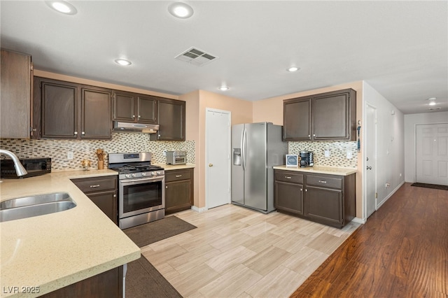 10253 Martinsburg Ct, Las Vegas, NV 89183 - kitchen featuring stainless steel appliances, under cabinet range hood, tasteful backsplash, dark brown cabinetry, and light wood-type flooring