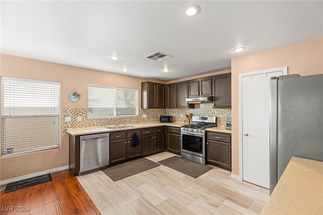 10253 Martinsburg Ct, Las Vegas, NV 89183 - kitchen with appliances with stainless steel finishes, under cabinet range hood, dark brown cabinetry, light countertops, and decorative backsplash