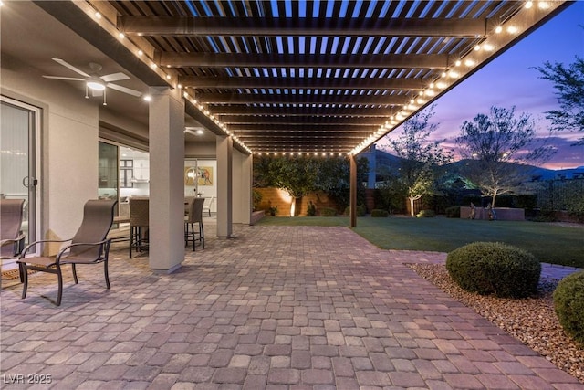 6338 Skystone St, Las Vegas, NV 89135 - patio terrace at dusk with a lawn, a pergola, ceiling fan, and a patio