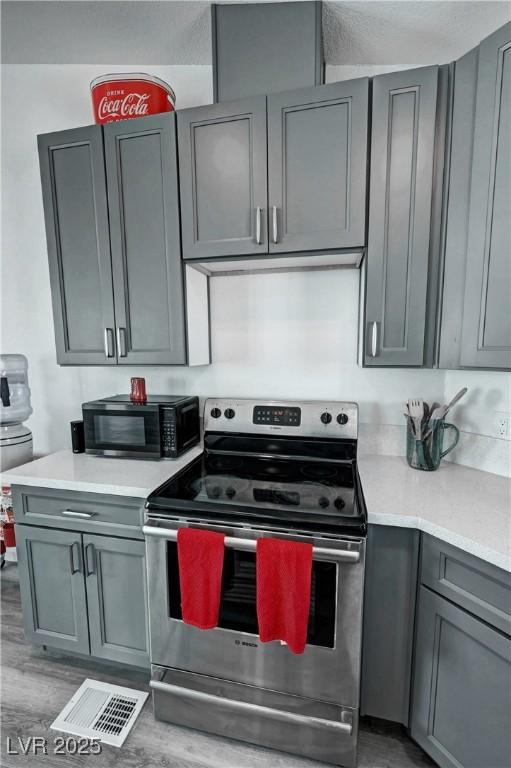 2530 Commercial Dr, Pahrump, NV 89048 - kitchen featuring stainless steel electric range, gray cabinets, black microwave, light countertops, and wood finished floors