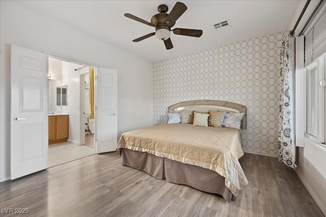 2117 Bay Thrush Way N, Las Vegas, NV 89084 - bedroom with wallpapered walls, an accent wall, light wood-type flooring, a ceiling fan, and connected bathroom