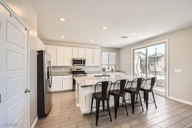 5606 Verde Valley Ct, North Las Vegas, NV 89081 - kitchen with appliances with stainless steel finishes, wood tiled floors, white cabinetry, light stone counters, and a center island with sink