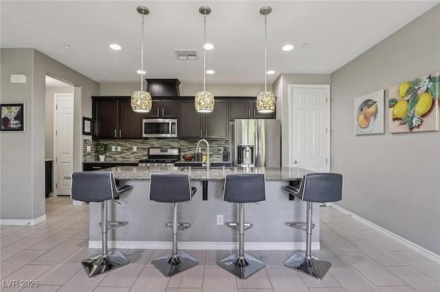 1922 Via Delle Arti, Henderson, NV 89044 - kitchen with appliances with stainless steel finishes, decorative backsplash, dark brown cabinetry, a kitchen bar, and recessed lighting