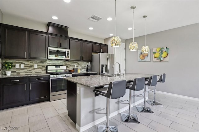 1922 Via Delle Arti, Henderson, NV 89044 - kitchen with appliances with stainless steel finishes, decorative backsplash, an island with sink, a kitchen bar, and light stone counters