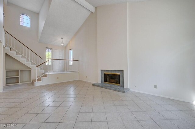 8809 Beach Front Dr, Las Vegas, NV 89117 - unfurnished living room featuring high vaulted ceiling, light tile patterned floors, stairs, beamed ceiling, and a glass covered fireplace