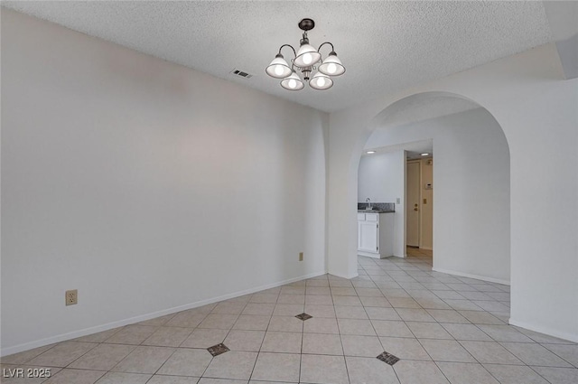 8809 Beach Front Dr, Las Vegas, NV 89117 - unfurnished room with arched walkways, a textured ceiling, a chandelier, and light tile patterned floors