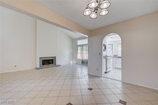 8809 Beach Front Dr, Las Vegas, NV 89117 - unfurnished living room with a textured ceiling, arched walkways, a chandelier, light tile patterned flooring, and a glass covered fireplace
