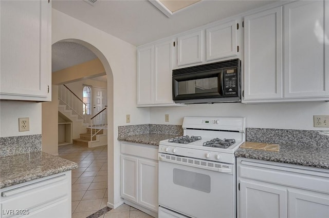 8809 Beach Front Dr, Las Vegas, NV 89117 - kitchen featuring white gas range, black microwave, light tile patterned floors, arched walkways, and white cabinetry