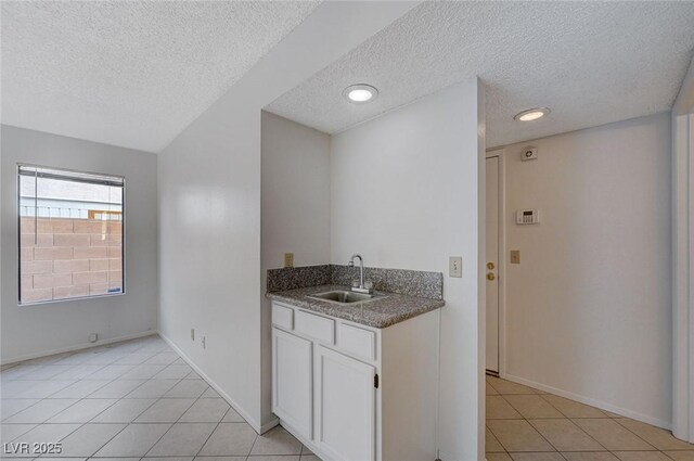 8809 Beach Front Dr, Las Vegas, NV 89117 - kitchen with a textured ceiling, light tile patterned floors, white cabinets, and dark stone countertops