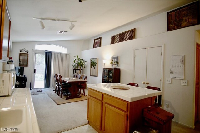 6131 Pumpkin Patch Ave, Las Vegas, NV 89142 - kitchen featuring tile counters, light colored carpet, track lighting, white microwave, and a center island