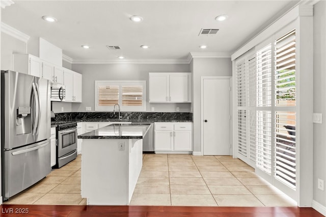 11649 Royal Derwent Dr, Las Vegas, NV 89138 - kitchen with appliances with stainless steel finishes, light tile patterned floors, white cabinetry, a kitchen island, and ornamental molding