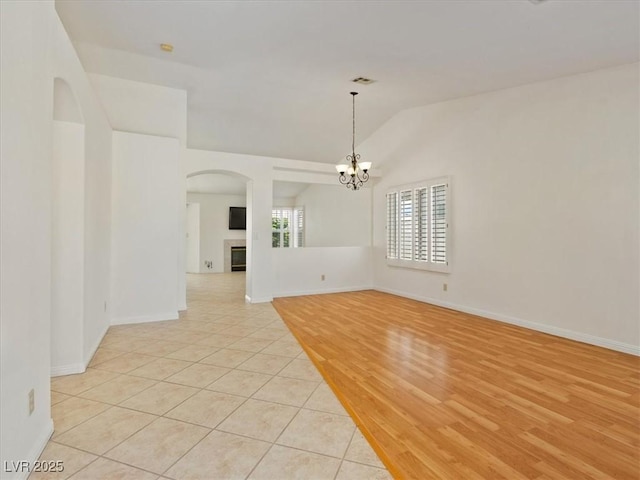 4323 Pageantry Falls Dr, North Las Vegas, NV 89031 - empty room with a chandelier, a fireplace, arched walkways, vaulted ceiling, and light tile patterned flooring