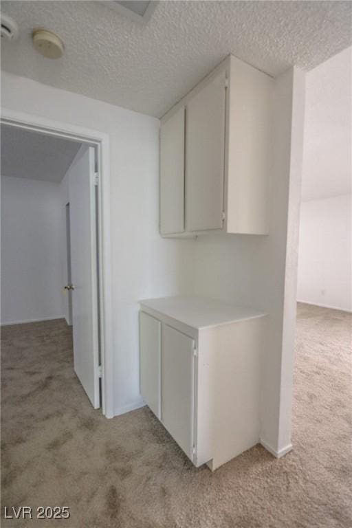 1349 Goldenglow Rd, Las Vegas, NV 89108 - kitchen with light colored carpet, light countertops, a textured ceiling, and white cabinetry