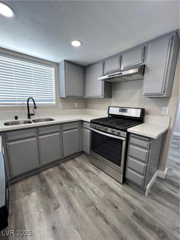 3238 Canyon Terrace Dr, Laughlin, NV 89029 - kitchen with stainless steel gas range, gray cabinetry, under cabinet range hood, light wood-style floors, and a textured ceiling