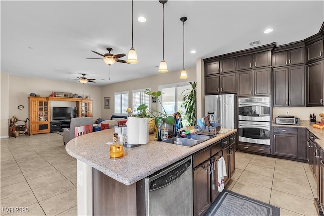 7854 Brianna Cheerful Ave, Las Vegas, NV 89178 - kitchen featuring appliances with stainless steel finishes, an island with sink, light tile patterned floors, dark brown cabinetry, and open floor plan