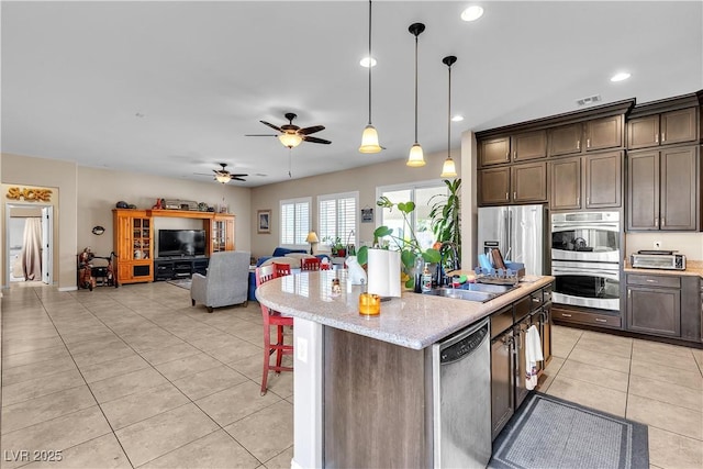 7854 Brianna Cheerful Ave, Las Vegas, NV 89178 - kitchen featuring appliances with stainless steel finishes, light tile patterned floors, dark brown cabinets, a center island, and hanging light fixtures