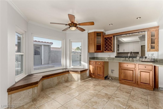 1393 Calmview Pl, Las Vegas, NV 89110 - kitchen featuring brown cabinetry, crown molding, glass insert cabinets, a ceiling fan, and light stone counters