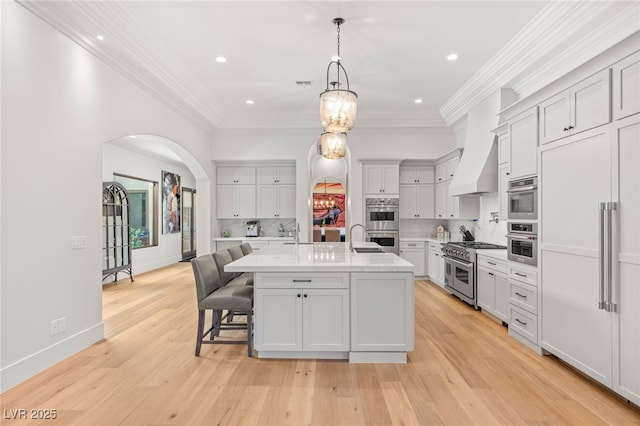 38 Pebble Dunes Ct, Las Vegas, NV 89141 - kitchen with premium appliances, arched walkways, light wood-style floors, a kitchen breakfast bar, and an island with sink