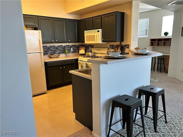 5855 Valley Dr Unit 2092, North Las Vegas, NV 89031 - kitchen featuring white appliances, a kitchen breakfast bar, backsplash, a peninsula, and light countertops