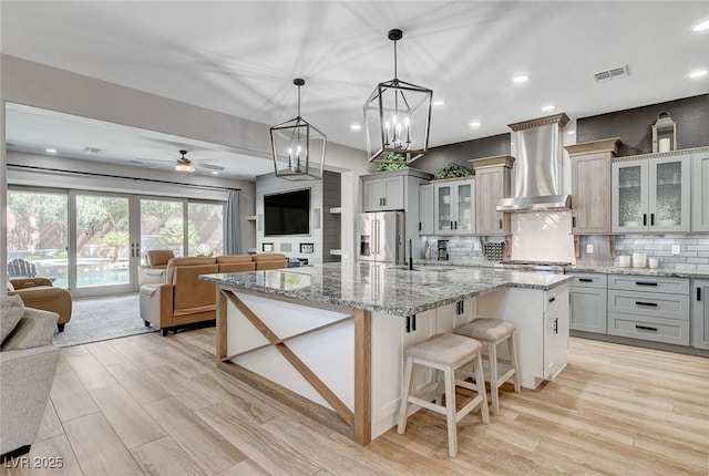 2333 Indigo Island St, Henderson, NV 89044 - kitchen with wall chimney range hood, open floor plan, stainless steel refrigerator with ice dispenser, a large island with sink, and recessed lighting