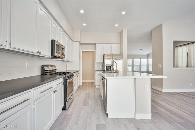 9514 Teton Vista Ave, Las Vegas, NV 89117 - kitchen featuring appliances with stainless steel finishes, light wood-style floors, decorative backsplash, recessed lighting, and a kitchen island with sink
