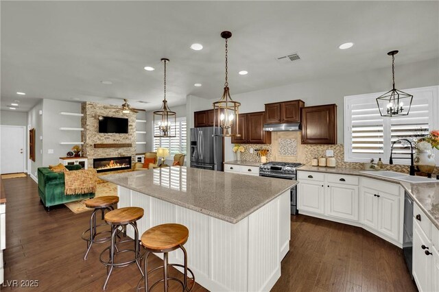 326 Caneflower Ct, North Las Vegas, NV 89031 - kitchen with appliances with stainless steel finishes, under cabinet range hood, a chandelier, a fireplace, and dark wood finished floors