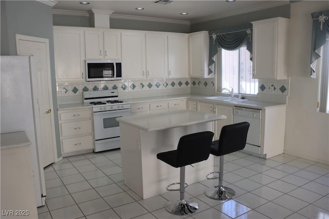 8982 Emerald Waters Ct, Las Vegas, NV 89147 - kitchen featuring white appliances, decorative backsplash, white cabinetry, a kitchen island, and crown molding
