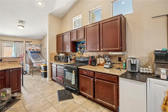 2716 Orchid Moon Ct, North Las Vegas, NV 89031 - kitchen featuring black gas range, decorative backsplash, light tile patterned floors, stainless steel microwave, and lofted ceiling