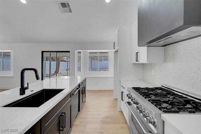 363 El Pico Dr, Henderson, NV 89014 - kitchen featuring wall chimney exhaust hood, appliances with stainless steel finishes, light countertops, light wood finished floors, and white cabinets