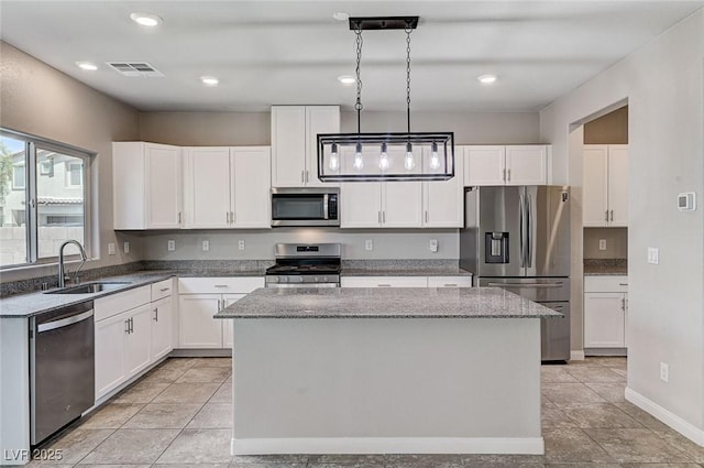 934 Twincrest Ave, North Las Vegas, NV 89032 - kitchen with appliances with stainless steel finishes, a kitchen island, white cabinetry, light stone counters, and decorative light fixtures