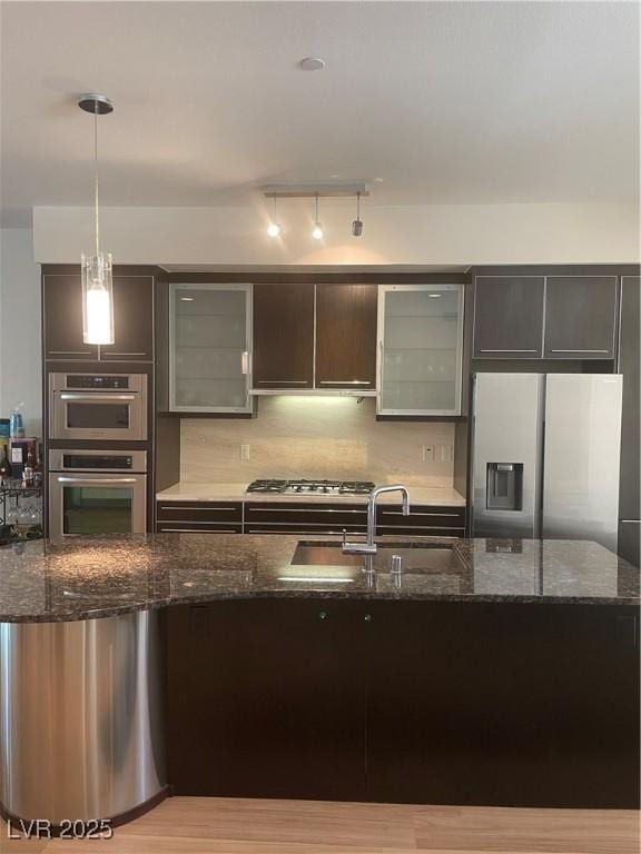 8925 W Flamingo Rd Unit 105, Las Vegas, NV 89147 - kitchen featuring appliances with stainless steel finishes, pendant lighting, dark stone counters, glass insert cabinets, and backsplash